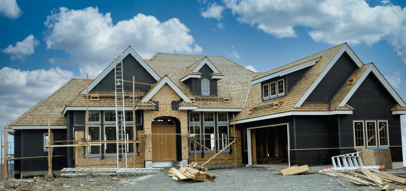New executive designed home under construction showing front exterior elevation, custom windows, roof peaks and dramatic puffy blue cloudy sky background. House front elevation stock images, royalty-free photos and pictures