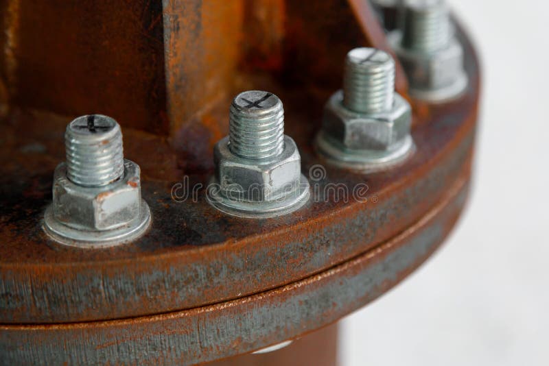 New galvanized bolts connect old rusty metal parts close-up on a light blurry background. The symbol of the unification of the