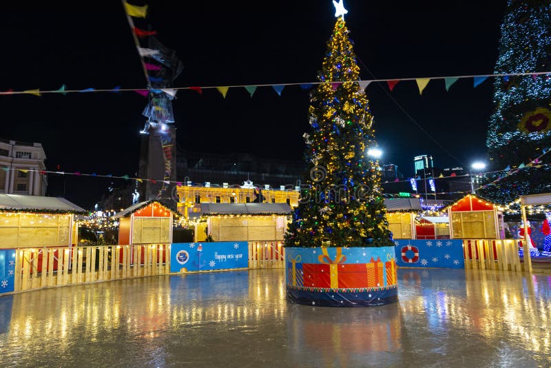 New year night scene. festive Christmas tree with decorations on the rink on the background of Christmas illumination and night sk