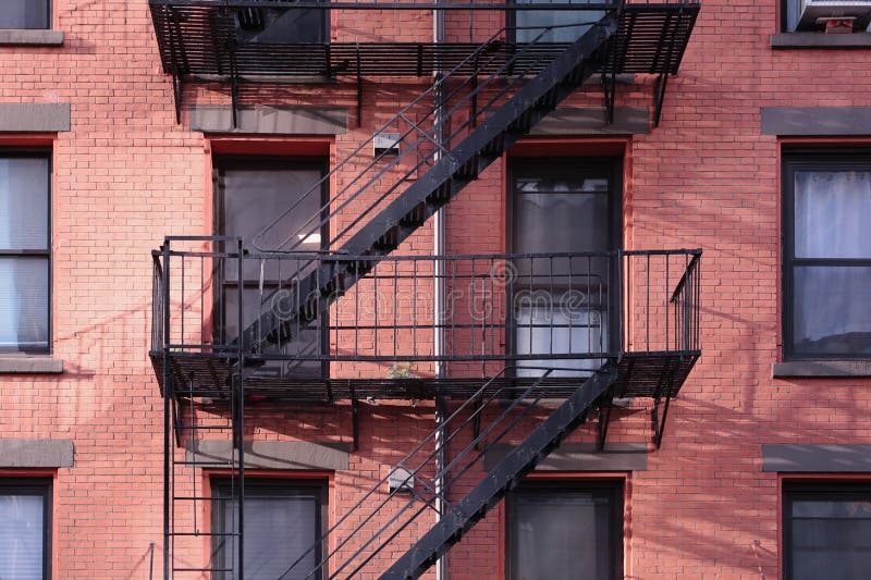 New York City apartment building painted red brick exterior, windows, and diagonal fire escape stairs