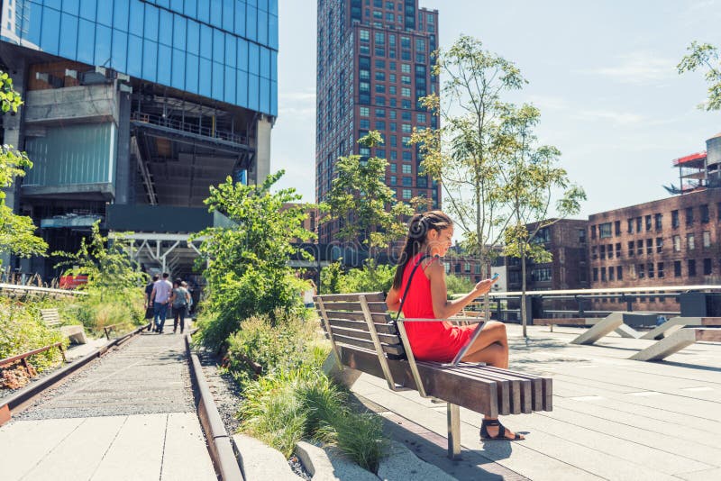 New York City lifestyle woman on mobile phone on urban high line park NYC. Tourist travel vacation girl sitting on