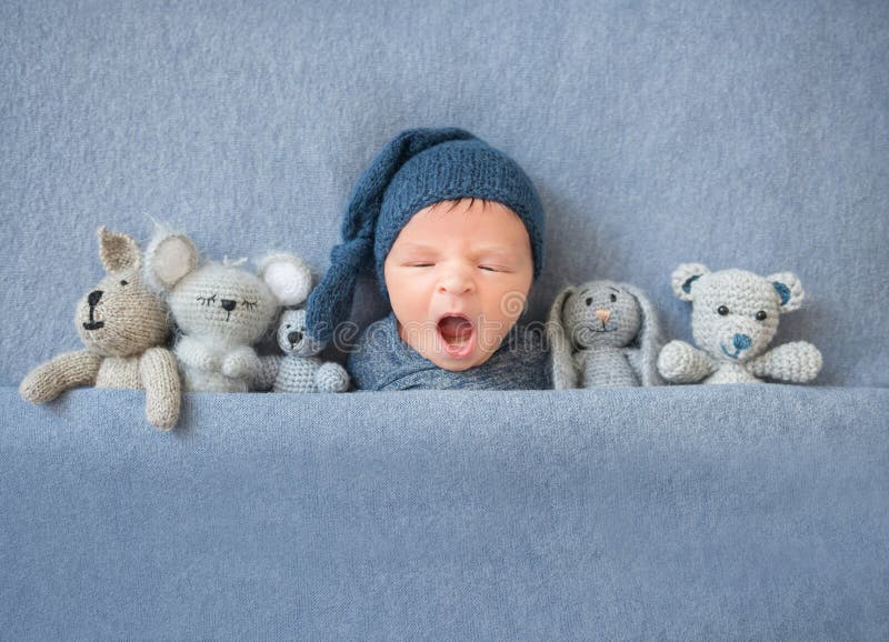 Newborn baby boy yawning and lying between plush toys