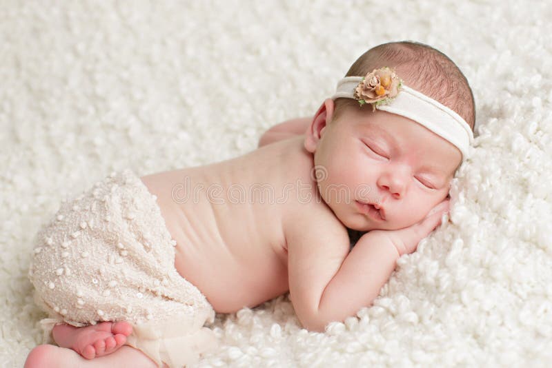 Baby girl wearing a skirt and headband sleeps peacefully with her hand lying under her face. Baby girl wearing a skirt and headband sleeps peacefully with her hand lying under her face