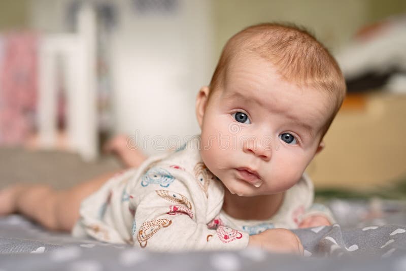 Newborn baby lies on his stomach, keeps his head on weight, drooling, droplets are visible on  lips,