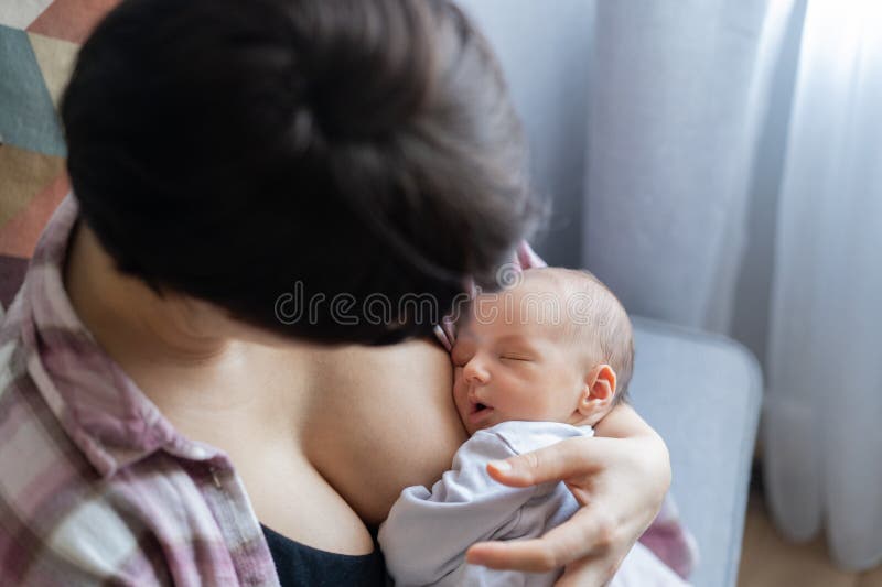 Newborn baby peacefully sleeping after breastfeeding in warm mother embrace at home. No face mother breastfeeding and royalty free stock images