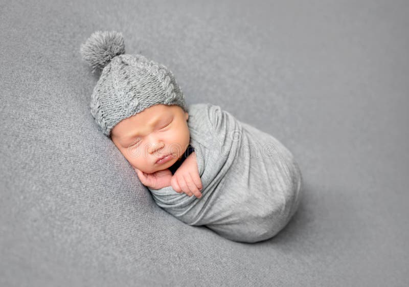 Newborn baby sleeping curled up in grey blanket