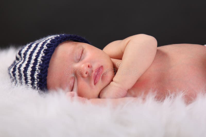 Un nuovo nato ragazzo dorme su un fuzzy coperta con un cappello a strisce.