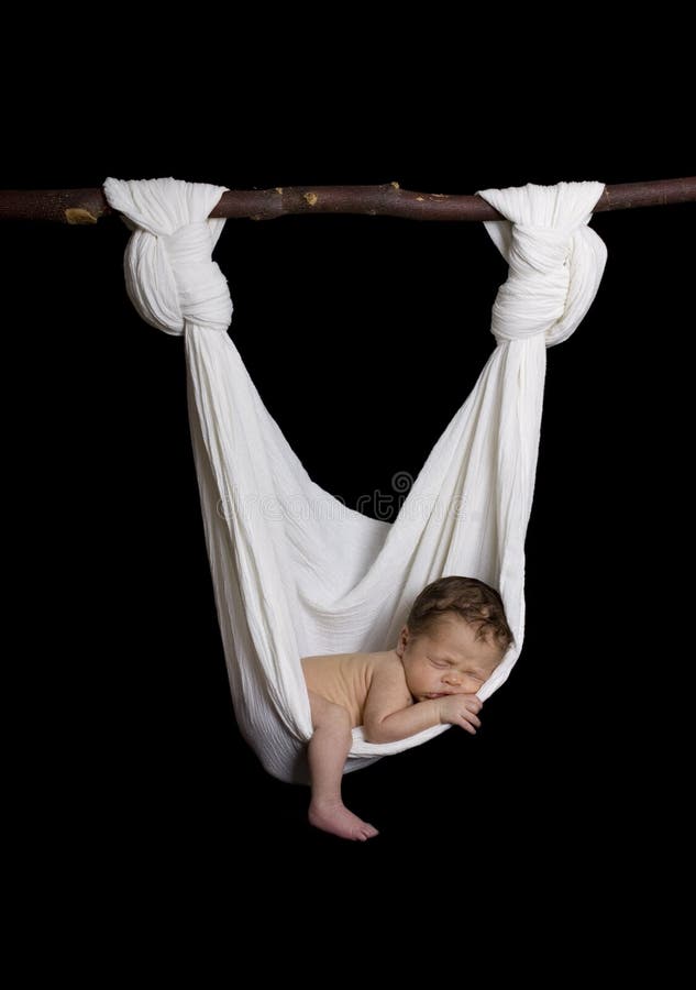 Newborn baby sleeping on its stomach looking very peaceful lying in a white hammock made out of cotton cloth and a wooden tree stick. black isolated background. Newborn baby sleeping on its stomach looking very peaceful lying in a white hammock made out of cotton cloth and a wooden tree stick. black isolated background.