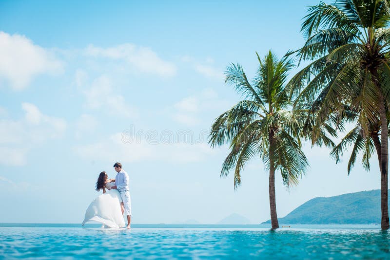 Newly married couple after wedding in luxury resort. Romantic bride and groom relaxing near swimming pool and sea. Honeymoon. Tropical country. Newly married couple after wedding in luxury resort. Romantic bride and groom relaxing near swimming pool and sea. Honeymoon. Tropical country.