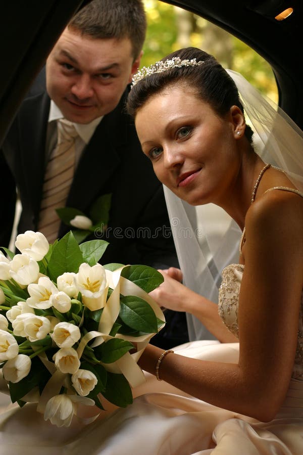 The groom helps the bride to leave from the automobile. The groom helps the bride to leave from the automobile