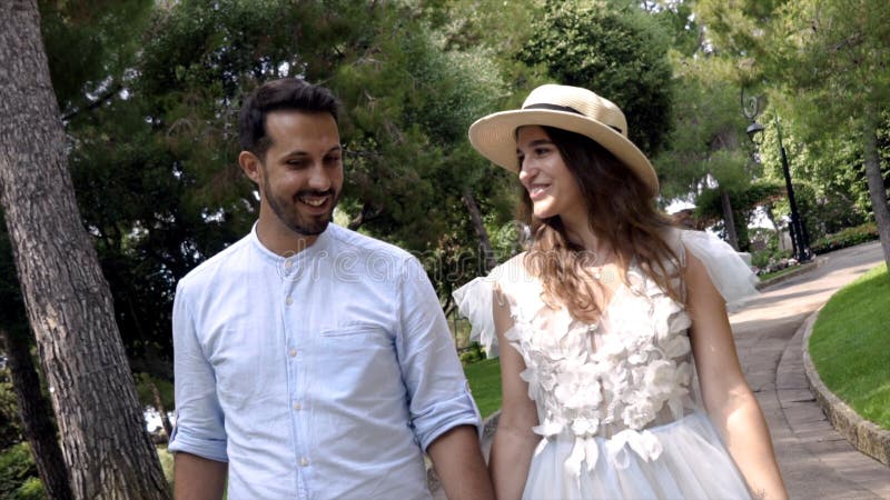 Newlyweds are smiling and holding hands in park. Action. Beautiful young couple beaming with happiness on honeymoon royalty free stock photo Newlyweds are smiling and holding hands in park. Action. Beautiful young couple beaming with happiness on honeymoon royalty free stock photo