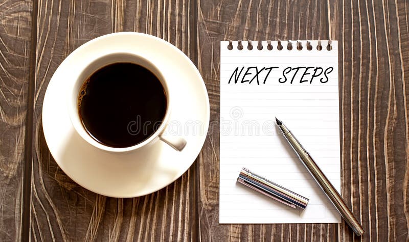 NEXT STEPS - white paper with pen and coffee on wooden background
