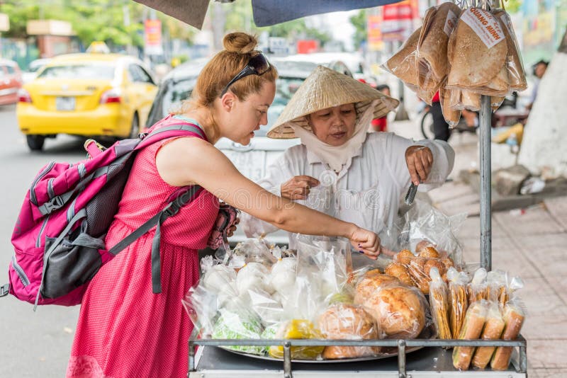 Nha Trang, Vietnam: en ensam kvinna som reser köper godis från en vietnamesisk försäljare av gatunärger royaltyfria bilder Nha Trang, Vietnam: en ensam kvinna som reser köper godis från en vietnamesisk försäljare av gatunärger royaltyfria bilder