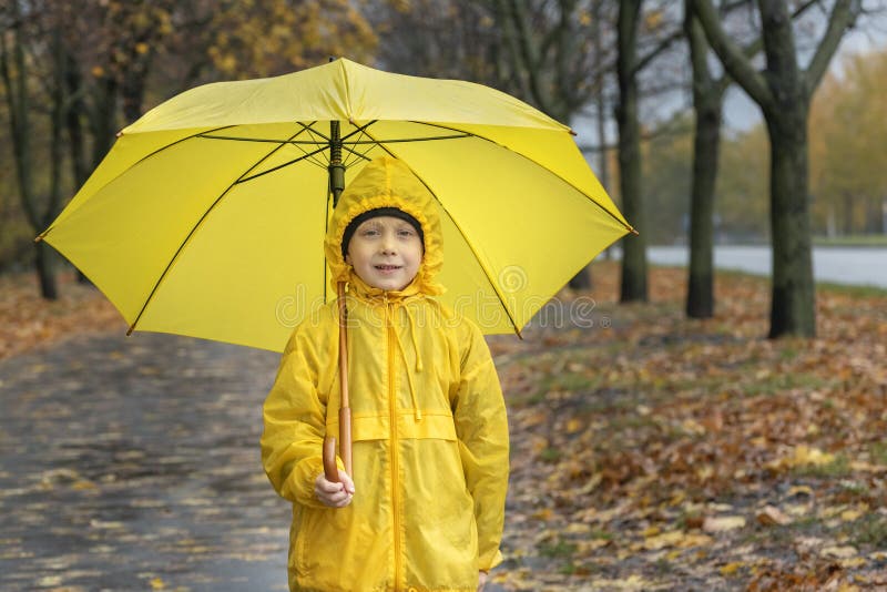 Niño Con Impermeable Amarillo Con Gran Paraguas Amarillo En Las Manos Sobre  Fondo Del Parque Otoñal. Retrato De Niño Caminando Imagen de archivo -  Imagen de agua, submarino: 260252283