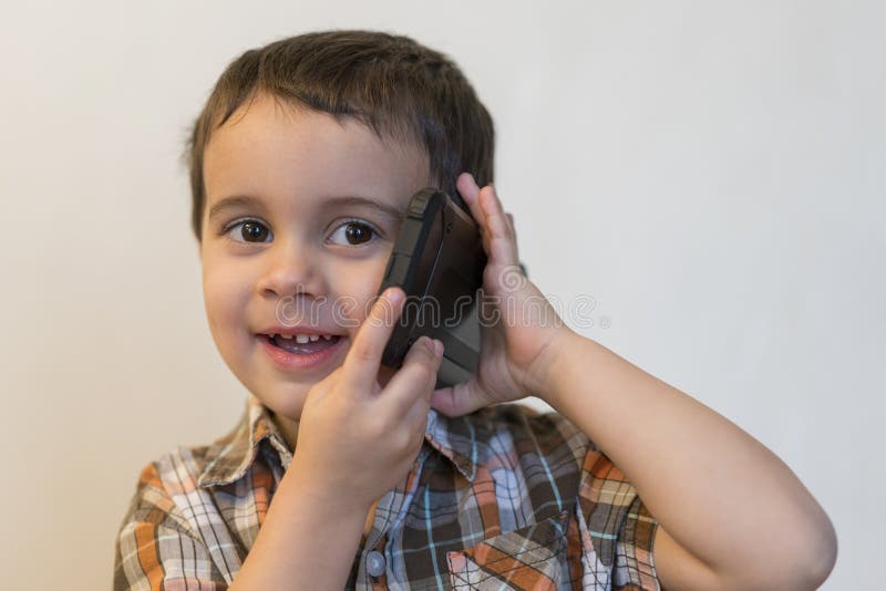 Ni?o peque?o lindo que habla por el tel?fono m?vil en fondo ligero Situaci?n feliz del ni?o peque?o y el hablar en smartphone en fotos de archivo libres de regalías Ni?o peque?o lindo que habla por el tel?fono m?vil en fondo ligero Situaci?n feliz del ni?o peque?o y el hablar en smartphone en fotos de archivo libres de regalías