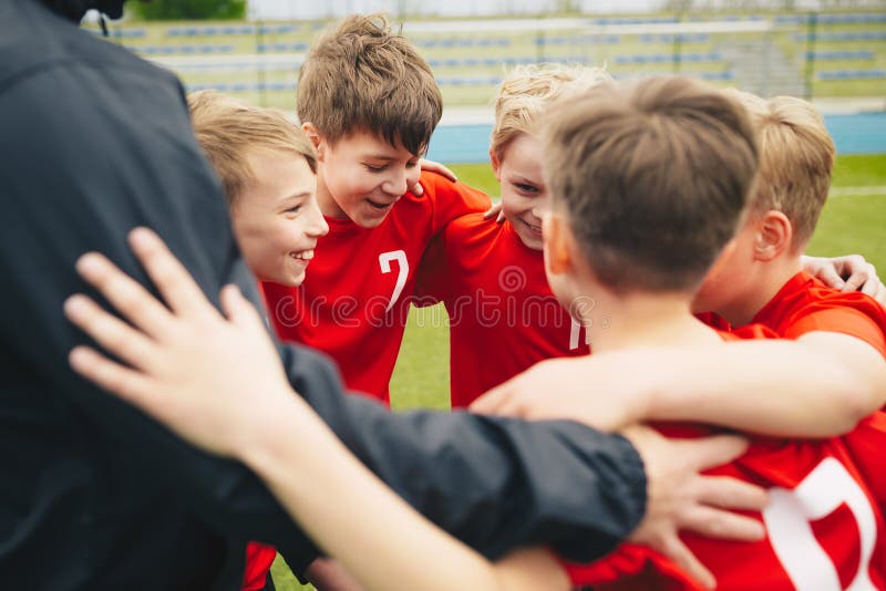 Ni? os felices que hacen deporte Grupo de muchachos felices que hacen el grupo de los deportes. Happy children making sport. Group of happy boys making sports huddle. Smiling kids standing together with coach on grass sports field. Boys talking with coach before the football game