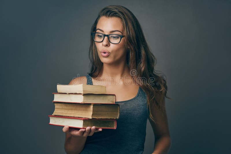 Nothing excites me like books. Studio shot of a young woman holding a pile of books against a grey background. Nothing excites me like books. Studio shot of a young woman holding a pile of books against a grey background