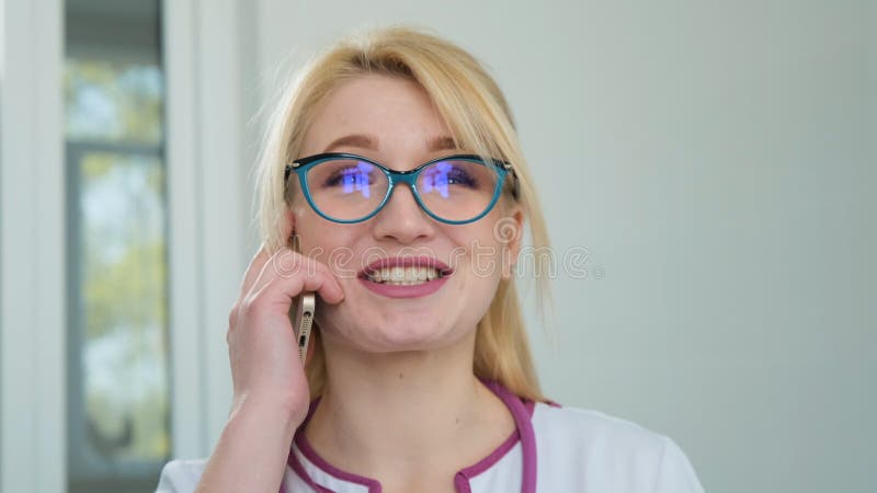 Nice blonde doctor in white coat smile and talking on phone. Positive mature woman physician talking on cell phone at