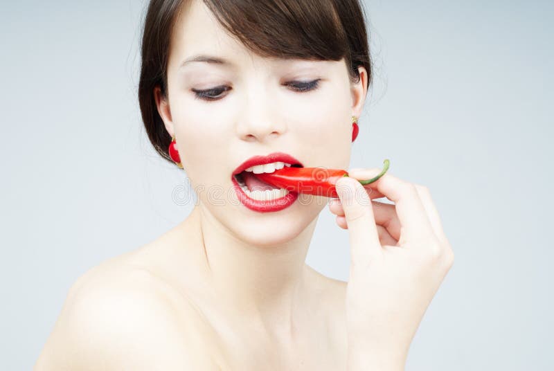 Nice brunette woman biting a chili pepper