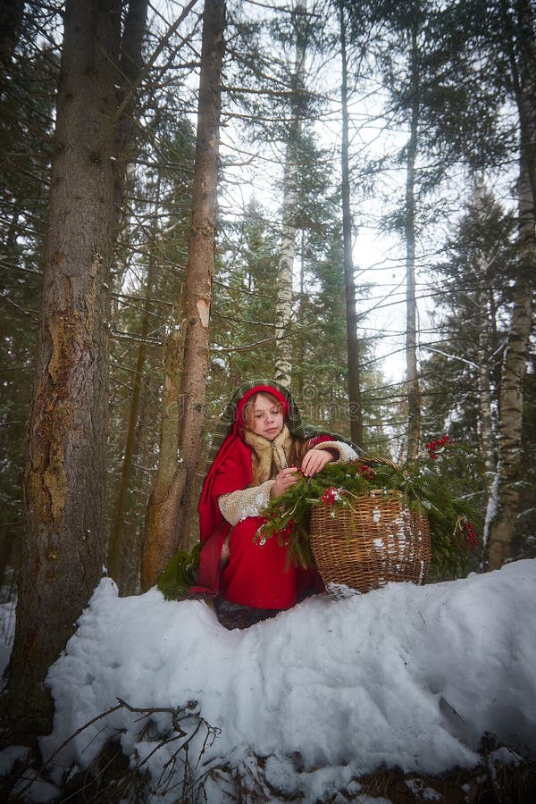 Nice cute teenager girl in old peasant clothes with hot fur coat and shawl in cold winter forest with fir trees, pines