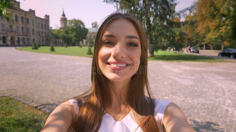 Nice de jonge vrouw zich in park in dag bevindt, houdt camera, maakt selfie, het glimlachen, communicatie concept