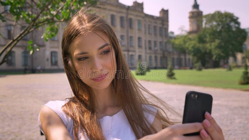 Nice de jonge vrouw zich in park in dag bevindt, maakt selfie op smartphone, het glimlachen, communicatie concept