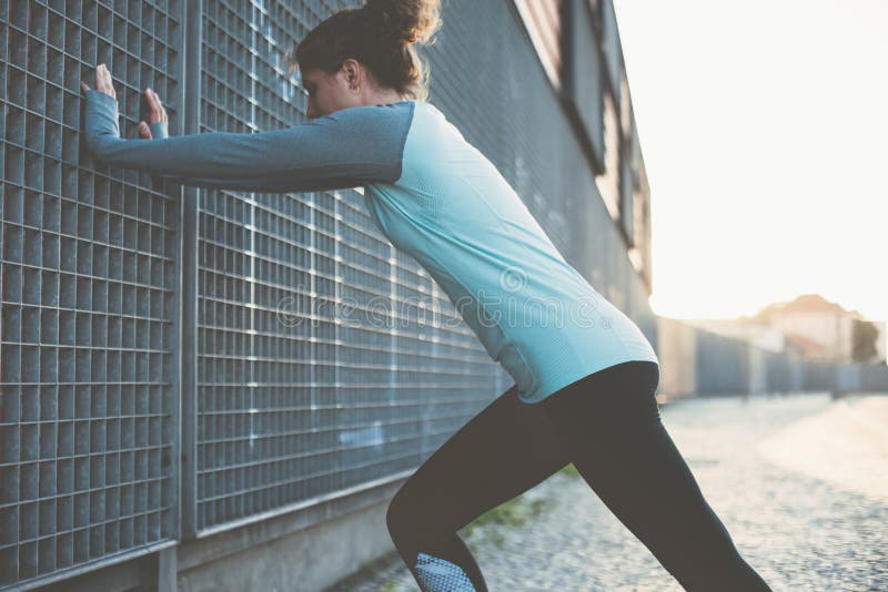 Nice and fit woman doing warming exercise on the street, safety stretching before workout.