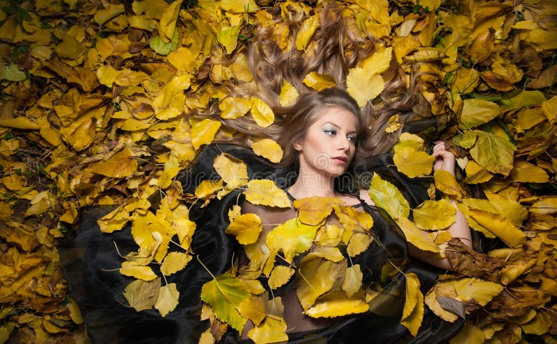 Nice girl covered with autumnal leaves. Young woman laying down on the ground covered by fall foliage in park. Beautiful girl. Lying on autumn leaves. Young stock photography Nice girl covered with autumnal leaves. Young woman laying down on the ground covered by fall foliage in park. Beautiful girl. Lying on autumn leaves. Young stock photography