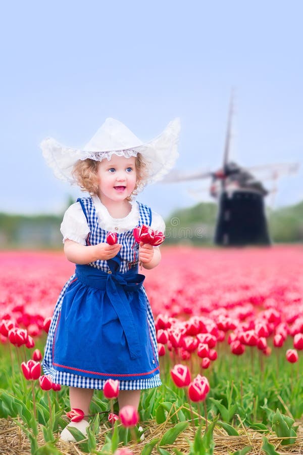 Nice girl in Dutch costume in tulips field with windmill