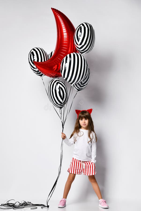 Full length of girl child with bunch of helium balloons.