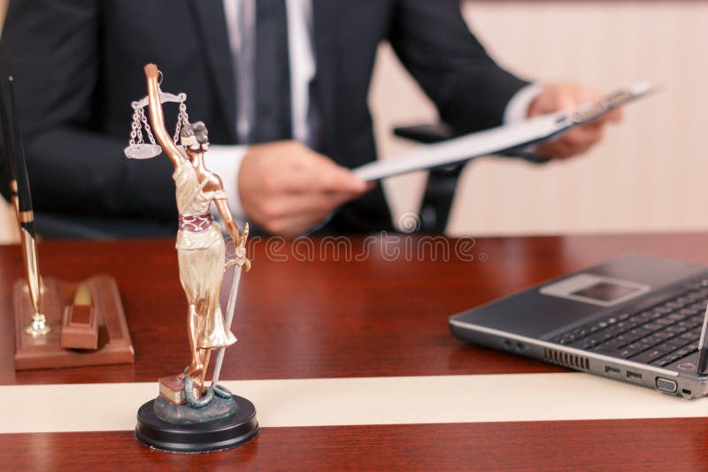 Law and equility. True lawyer sitting at the table and holding papers with statue of justice on forefront. Law and equility. True lawyer sitting at the table and holding papers with statue of justice on forefront