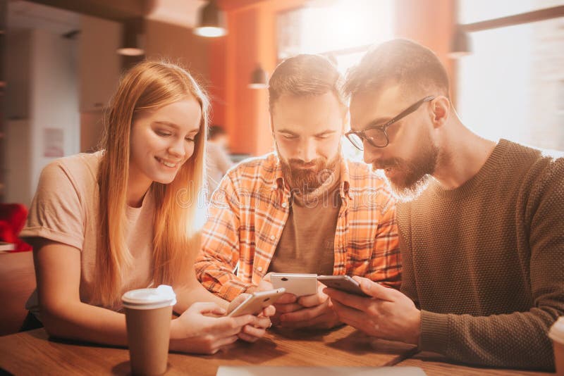 Nice picture of three friends sitting together and holding phones in their hands. They are playing games. This people stock photos Nice picture of three friends sitting together and holding phones in their hands. They are playing games. This people stock photos