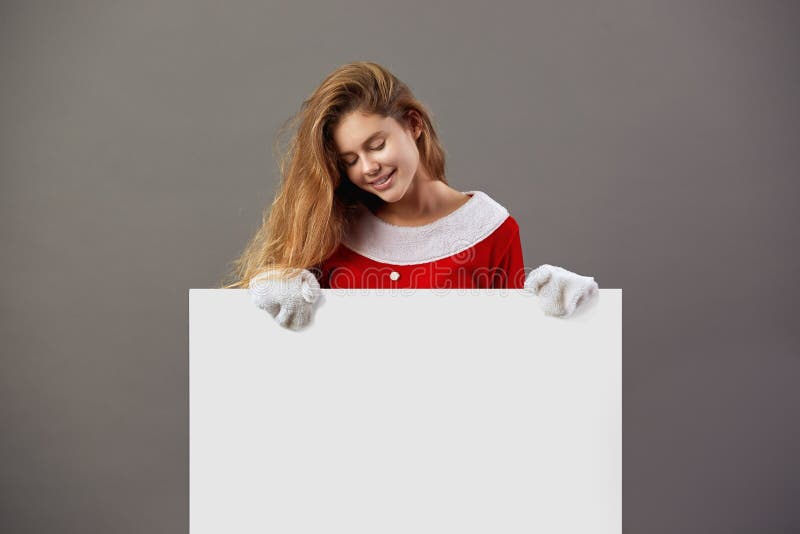 Nice young mrs.Santa Claus dressed in the red robe and white gloves holds the white canvas in front of her on the gray stock image Nice young mrs.Santa Claus dressed in the red robe and white gloves holds the white canvas in front of her on the gray stock image