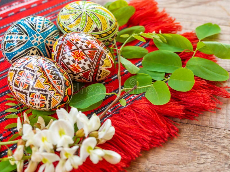 Nicely hand decorated romanian orthodox easter eggs with traditional motifs on a red cloth with acacia flowers aside