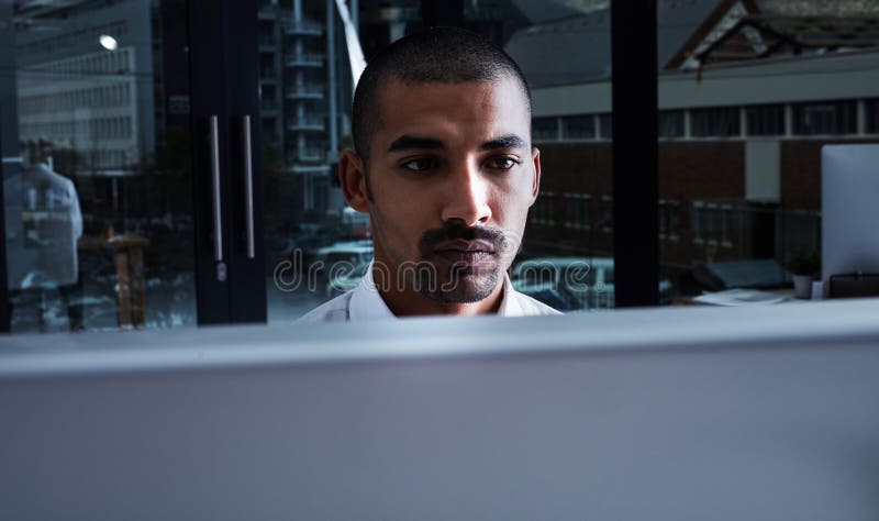 Hes not here to be average. a young businessman using a computer at night in a modern office. Hes not here to be average. a young businessman using a computer at night in a modern office