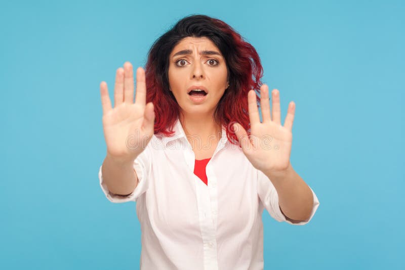 No, I`m afraid! Portrait of scared stressed woman with fancy red hair in white shirt gesturing stop and shouting from fear, afraid of sudden threat. indoor studio shot  on blue background. No, I`m afraid! Portrait of scared stressed woman with fancy red hair in white shirt gesturing stop and shouting from fear, afraid of sudden threat. indoor studio shot  on blue background