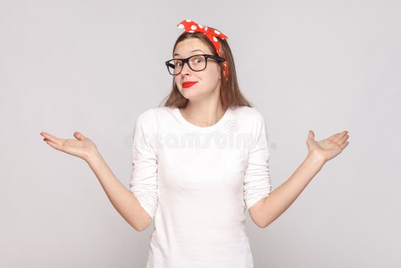 I dont know. i have no idea. portrait of beautiful emotional young woman in white t-shirt with freckles, black glasses, red lips and head band. indoor studio shot, isolated on light gray background. I dont know. i have no idea. portrait of beautiful emotional young woman in white t-shirt with freckles, black glasses, red lips and head band. indoor studio shot, isolated on light gray background.