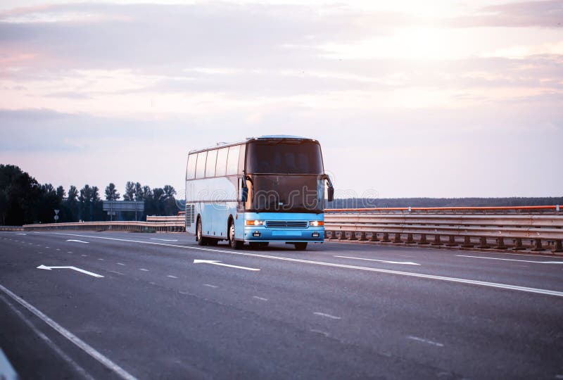 Niebieski komfortowy autobus przewozi pasażerów wzdłuż autostrady wieczorem z włączonymi światłami. koncepcja podróży obrazy royalty free
