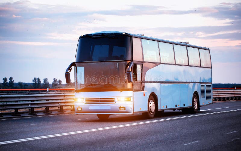 Niebieski komfortowy autobus przewozi pasażerów wzdłuż autostrady wieczorem z włączonymi światłami. koncepcja podróży zdjęcia stock