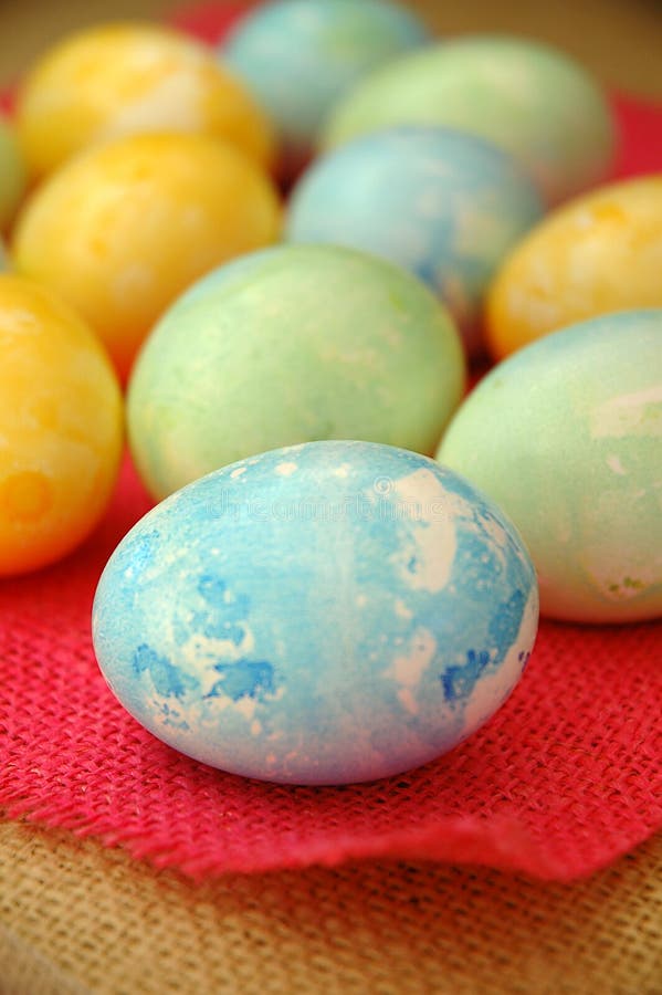 A blue Easter egg sitting on dyed pink and natural burlap a with a dozen colored eggs behind. A blue Easter egg sitting on dyed pink and natural burlap a with a dozen colored eggs behind.