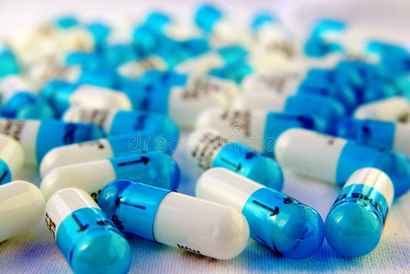 About 50 white and blue medication capsules spread on a white surface. About 50 white and blue medication capsules spread on a white surface