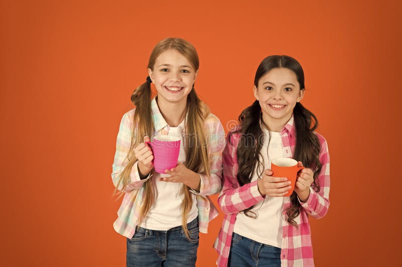 Make sure kids drink enough water. Girls kids hold cups orange background. Sisters hold mugs. Drinking tea while break. Relaxing with drink. Tea break. Children do not drink enough during school day. Make sure kids drink enough water. Girls kids hold cups orange background. Sisters hold mugs. Drinking tea while break. Relaxing with drink. Tea break. Children do not drink enough during school day.