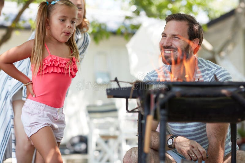 Niedlich kleine Mädchen weht zu einem Feuer für Grill mit ihren Eltern