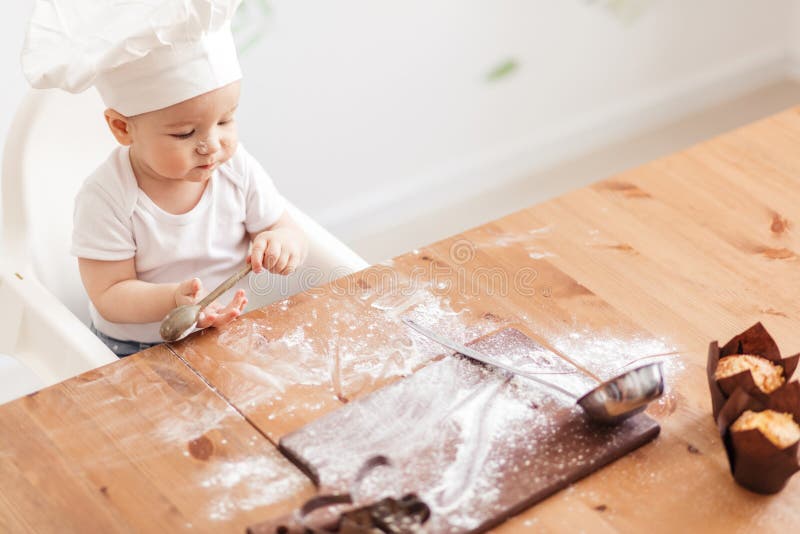 Niemowlaka dziecka kucbarski portret jest ubranym białego szefa kuchni kapelusz przy kuchennym stołem fotografia stock