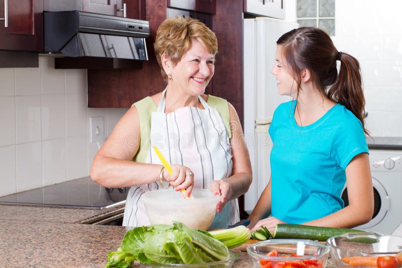 Happy grandma talking to granddaughter in kitchen while cooking. Happy grandma talking to granddaughter in kitchen while cooking