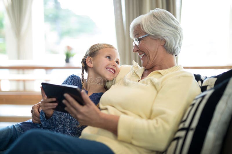 Nieta y abuela sonrientes que usa la tableta digital en el sofá imagen de archivo libre de regalías