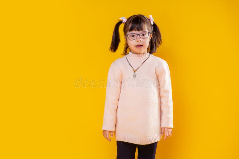 Nieuwsgierig meisje met het benedensyndroom stellen tegen oranje muur royalty-vrije stock foto Nieuwsgierig meisje met het benedensyndroom stellen tegen oranje muur royalty-vrije stock foto