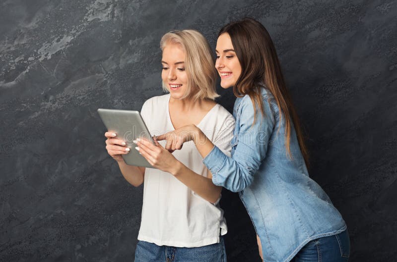 Nieuwsgierige vrouwelijke vrienden die tablet gebruiken bij donkere studioachtergrond stock foto Nieuwsgierige vrouwelijke vrienden die tablet gebruiken bij donkere studioachtergrond stock foto