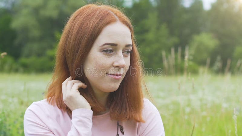 Nieśmiali piękni kobiet spojrzenia zestrzelają w górę outdoors w lata polu, czerwona z włosami kobieta