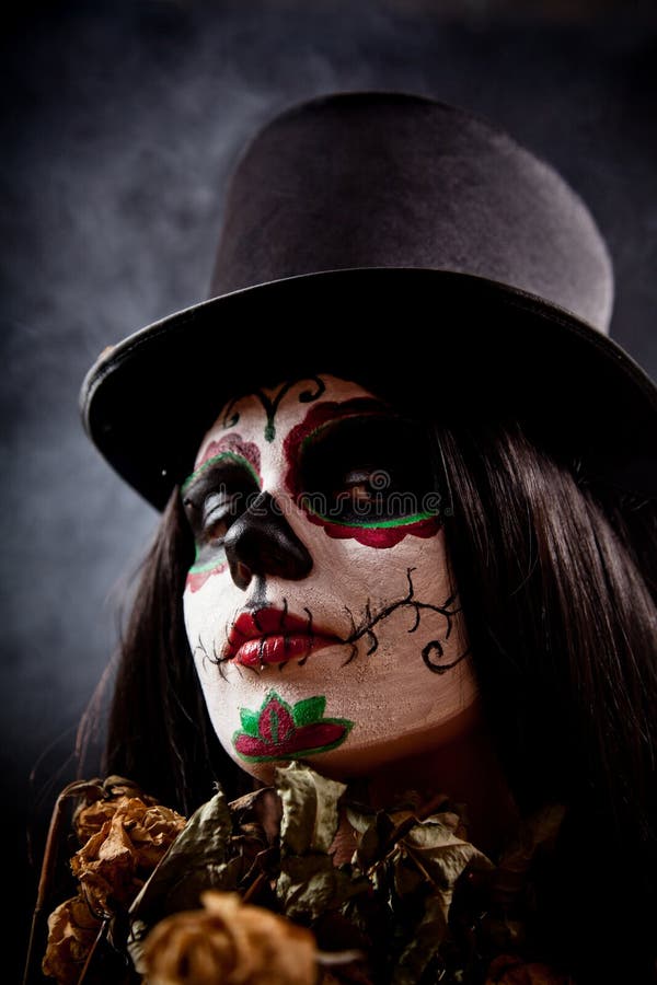 Sugar skull girl in tophat holding dead roses, studio shot. Sugar skull girl in tophat holding dead roses, studio shot